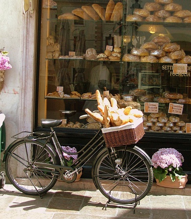 Bread Delivery Bike in Italy with bread in its basket. The background is a bakery window with a variety of bread loaves.