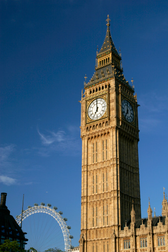Big Ben with bridge over Thames and flag of England against blue sky in London, England, UK