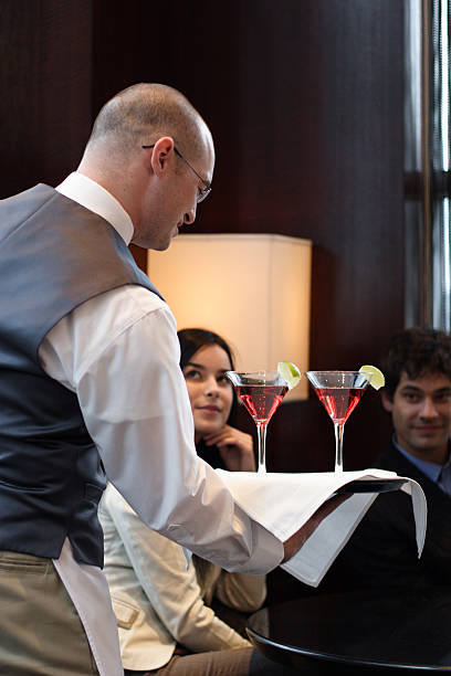Waiter delivering cocktails to couple stock photo