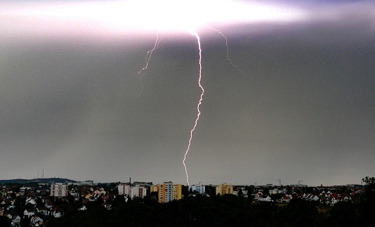 Evening twilight and a single nearly vertical lightning comes down at the buildings