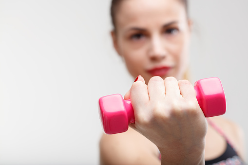 Blurred woman lifting pink weights, enhancing her happiness and day. A light workout at the gym provides positive psychological effects
