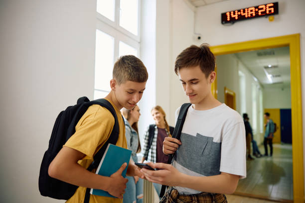 istock Happy high school students using mobile phone on a break in hallway. 1571673340