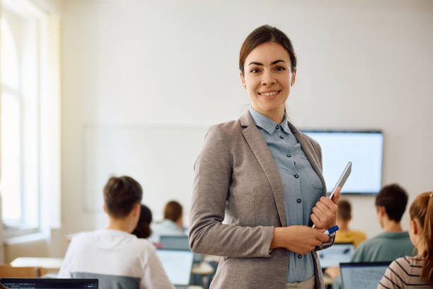 istock Smiling IT teacher during computer class at high school and looking at camera 1571675470