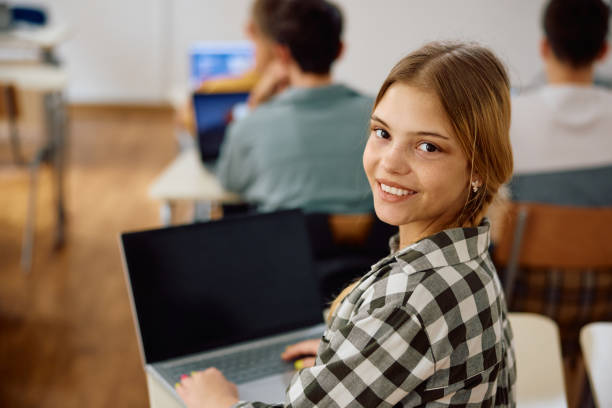istock Happy female student using laptop on computer class at high school and looking at camera. 1571675995
