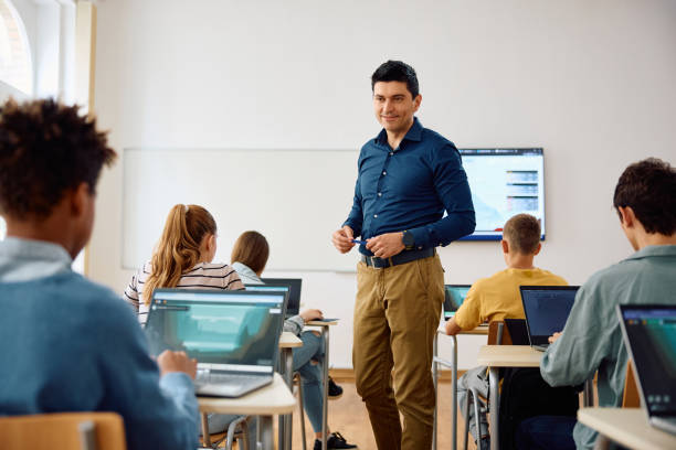 istock Happy high school teacher and his students during computer class in the classroom. 1571676012