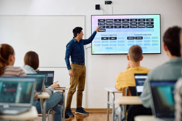 High school teacher using smartboard while teaching students in the classroom. Male teacher using interactive whiteboard while giving a lesson to high school students in the classroom. male teacher white board stock pictures, royalty-free photos & images
