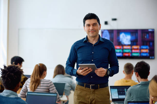 istock Happy high school teacher in the classroom looking at camera. 1571676526