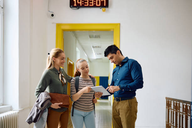 istock High school teacher using touchpad with his student and her mother in a hallway. 1571677810