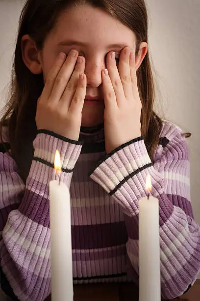 Girl says the blessing over the Shabbos candles. Per tradition, she covers her eyes.