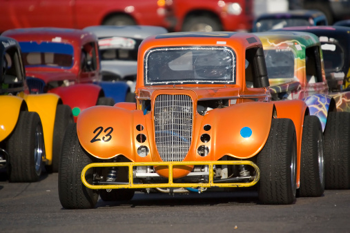 A bright orange midget race car lines up at the starting line along with several other brightly colored race cars.