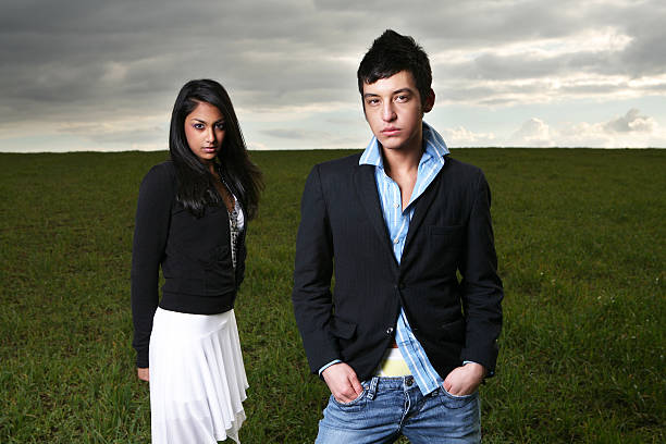 Young beautiful couple wearing casual t-shirt standing over isolated white background clueless and confused expression with arms and hands raised. Doubt concept.