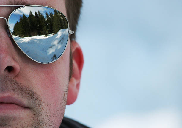 The Man in Mirrored Sunglasses Half of a man's face wearing reflective sunglasses with a stubble beard. Reflection shows trees and snow. aviator glasses stock pictures, royalty-free photos & images