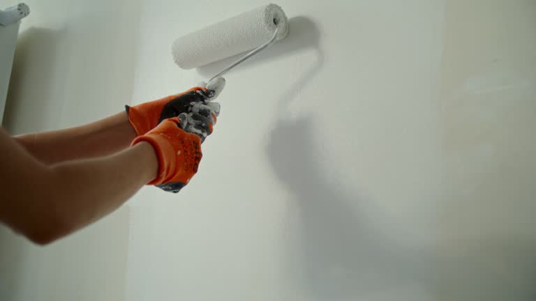 Close-up young woman painting her dream house walls with a roller. Wearing protective clothes and goggles