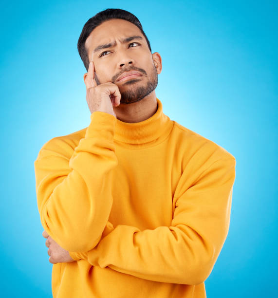 istock Thinking, idea and young man in a studio with doubt, confused or choice facial expression. Problem solving, dream and Indian male model brainstorming, question or planning isolated by blue background 1571782531