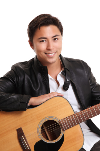 Young singer songwriter with an acoustic guitar sitting down. Wearing a white shirt with jeans and a black leather jacket. White background.