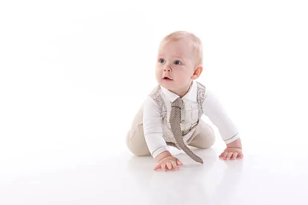 Smiling baby in a beige romper suit and tie crawling. On a white background with reflection