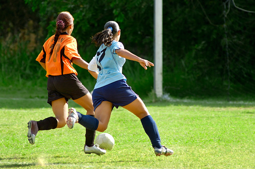 Two soccer girls chasing the ball  captured in perfect synchronization few inches above the field while running in a game.