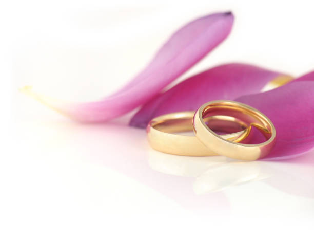 Two classic gold wedding rings surrounded by pearl beads, small delicate flowers on white satin with waves of fabric. top view. postcard. invitation