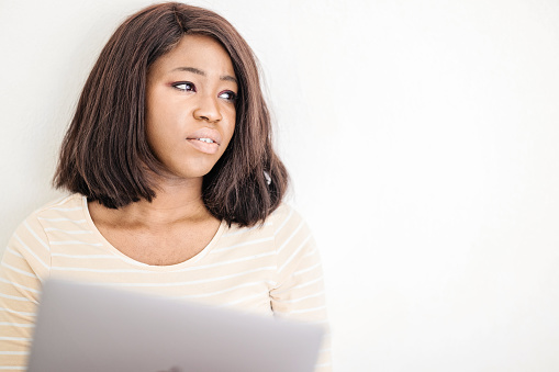 Black woman deep in thought looking sideways while holding laptop