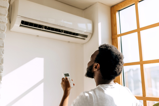 Rear view of young man turning on air conditioner at home