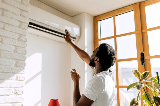 Rear view of young man turning on air conditioner at home