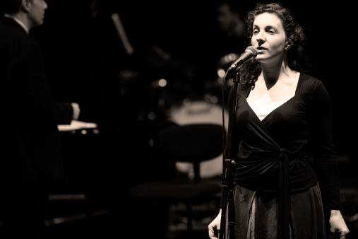 Solo female vocalist on stage with elements of a big band visible in the background.
