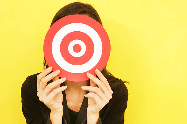 A woman in black against a yellow backdrop holding a target stock photo