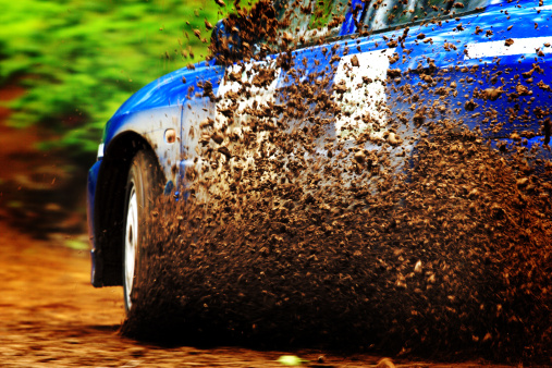 A car sprays mud as it zips around a corner in a dirt road rally