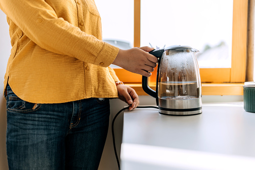 Close up shot of an unrecognisable woman using kettle in kitchen