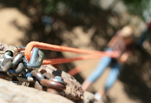 Detailed photo of a rope afixed to a rock climbing tie down.  The climber is visible in the blurred background.