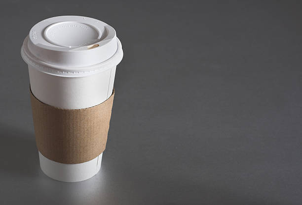 Image of white sticker on paper cup of latte or cappuccino with patterned heart latte art on a wooden table. Concept of serving coffee to take away, coffee to go.