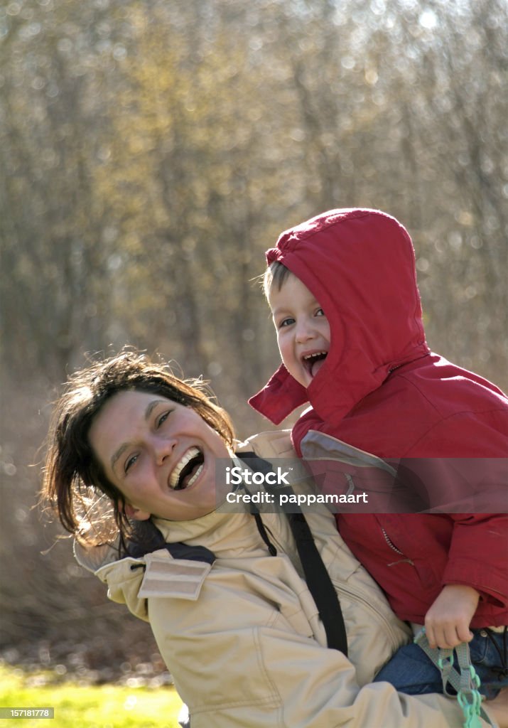 Rindo mulher carregando seu filho em pé em frente a árvores - Foto de stock de 2-3 Anos royalty-free