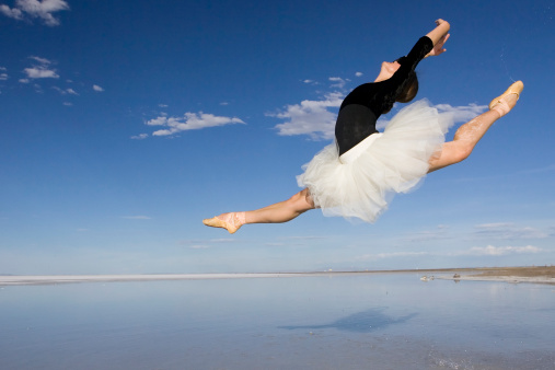 A ballerina performs over water on the deserted Salt Flats of Utah against a deep blue sky.