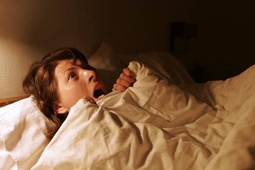 A woman in the bed in the dark expressing fear