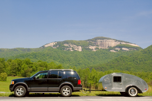 A teardrop camper trailer behind an SUV parked on the roadside with Table Rock, SC, in the background.