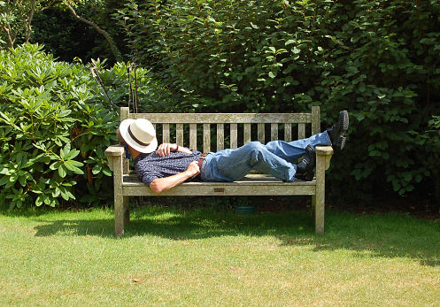 Man asleep on a bench in a garden under a hat