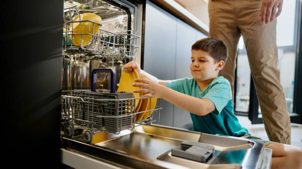istock Little boy taking out dishes from a dishwasher 1571828249