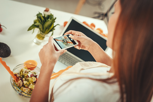 Beautiful young woman taking photo of healthy salad with smartphone for her vlog.