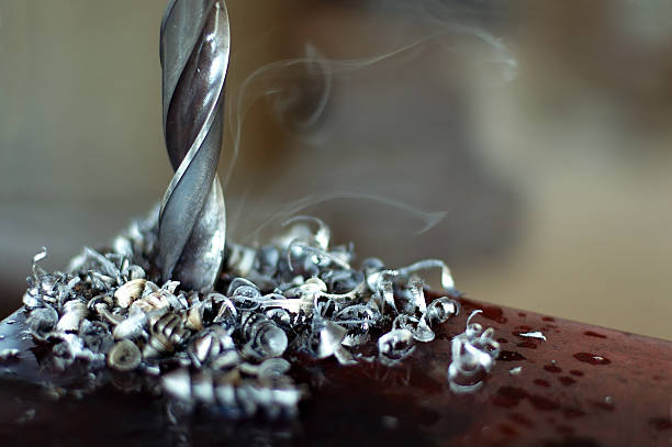 A silver drill turning with metal shavings and smoke stock photo