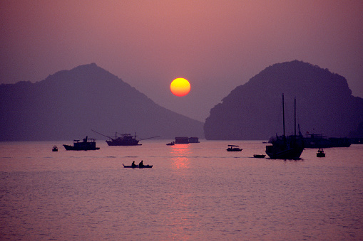 Sunset and Boats, Ha Long Bay, Vietnam -- view from Cat Ba Island -- sun setting in violet light, between two hills.