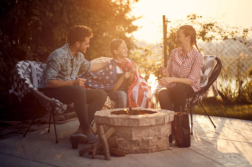 Family gathers around a crackling fire, joyfully roasting marshmallows as they celebrate Independence Day. The scene exudes a sense of warmth, togetherness, and patriotic spirit.