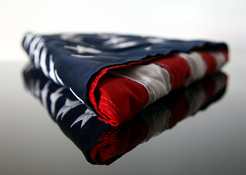 Close up of a folded american flag on a reflective surface.  Focus is on the closest portion of the flag with a shallow depth of field.