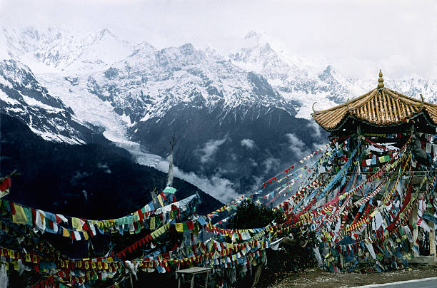 Colorful prayer flags are set up in a mountainous area under a cloudy sky, showcasing a blend of nature and religious elements.