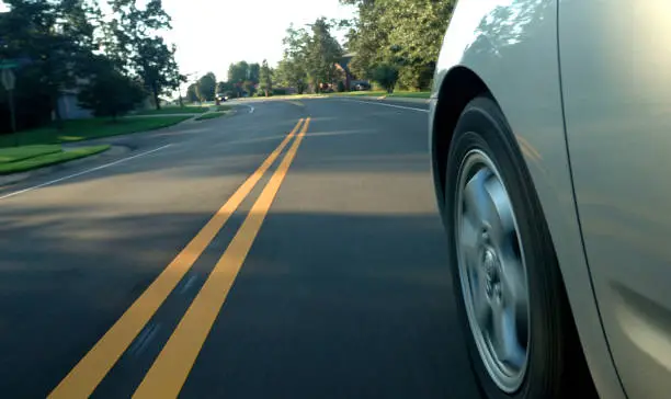 Unusual view of car traveling down a suburban road, blurred hubcap and street foreground indication motion