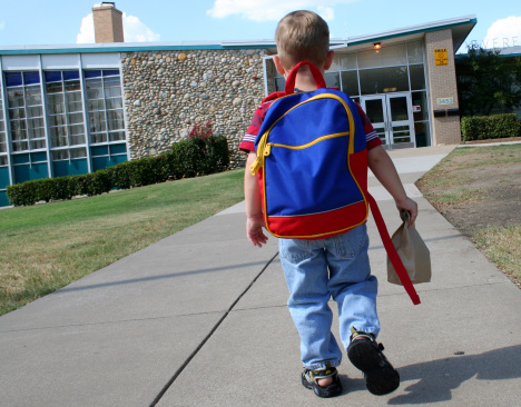 Young Elementary Schoolboy  walking up to school carrying backpack and brown bag for lunch or show/tell.