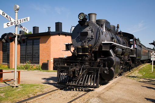 A steam locomotive pulling a passenger train through a railway crossing.