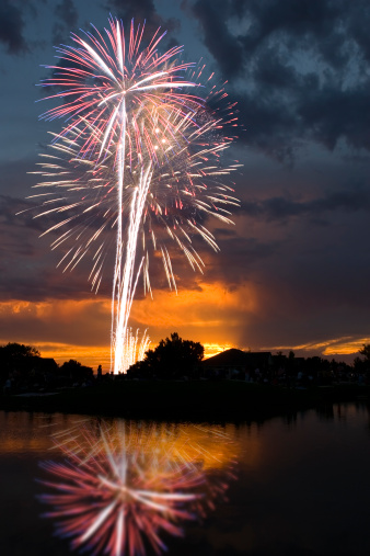 Fireworks celebration reflected in a lake on July 4th, independence Day, against a beautiful sunset.