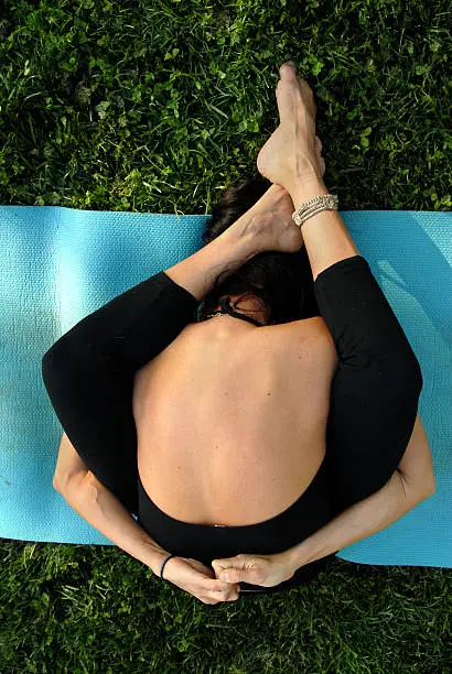 Girl in the tortoise pose of yoga on a mat on a lawn