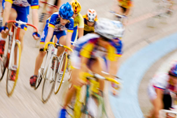 Professional cyclists racing in peloton formation around a velodrome a pack of cyclists hurtle around the banked curve of a velodrome. velodrome stock pictures, royalty-free photos & images