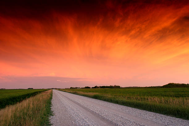 A gravel road on the plains. Prairie scenic with dramatic sunset sky. Rural landscape in the Midwest. Summer season with agriculture the main industry on these flat plains. 